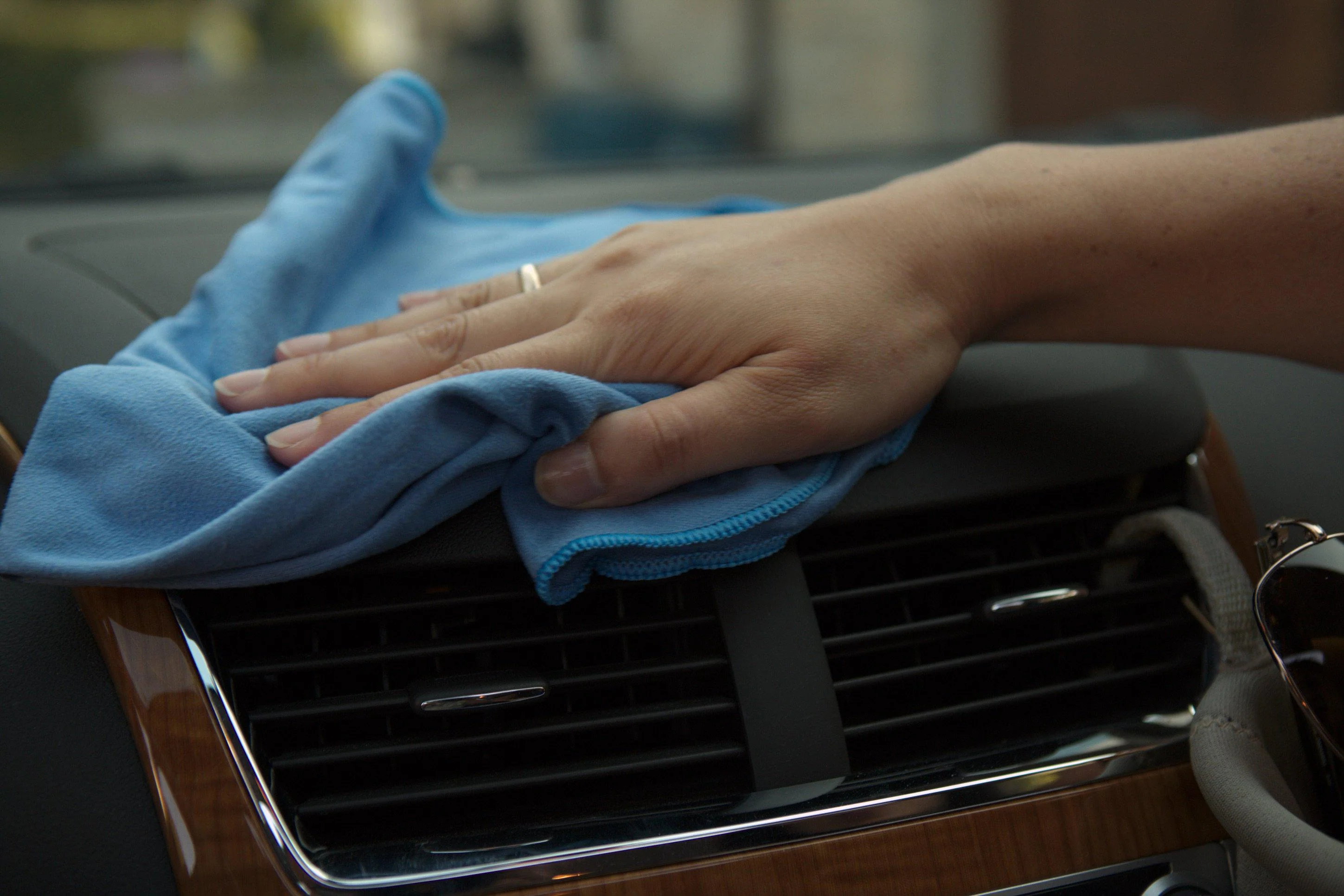 A close-up of a hand wiping a car dashboard with a clean microfiber towel, steering wheel visible in the foreground