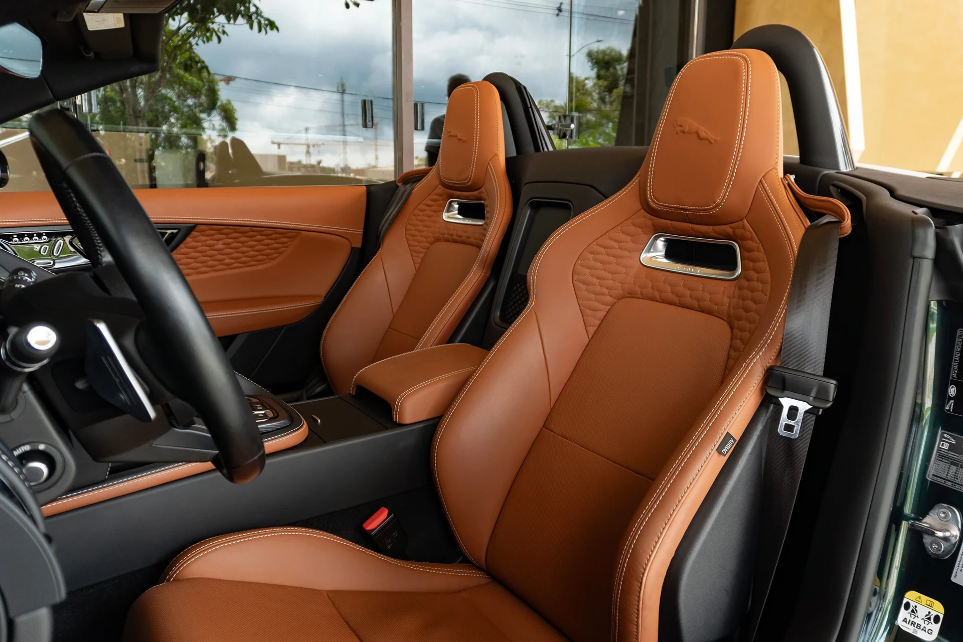 A person cleaning a tan leather car seat with a microfiber towel, focusing on the seat cushion and stitching
